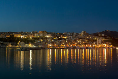 Illuminated buildings by river against clear sky at night