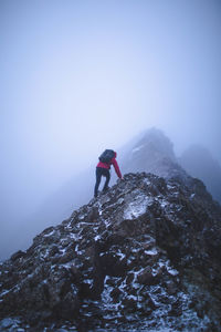 Man climbing rock on mountain against sky