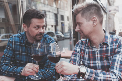 Gay couple toasting red wine while sitting at outdoor restaurant