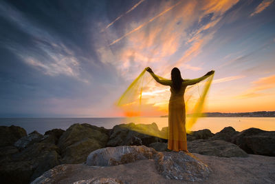 Woman in a yellow dress and cape observing a magnificent sunrise on the french basque coast v