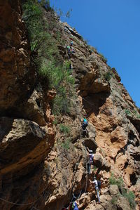 Low angle view of people on rock formation against sky