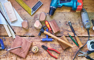 Top view of electric screwdriver near pliers with chisel and wooden blocks in artisan workshop