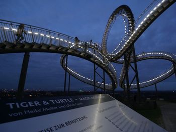 Information sign by illuminated tiger and turtle  magic mountain against sky at dusk