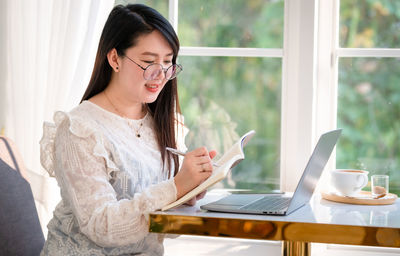 Young woman using mobile phone while sitting on table