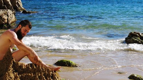 Full length of shirtless man making castle at beach