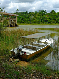 Abandoned boat moored on field by lake against sky