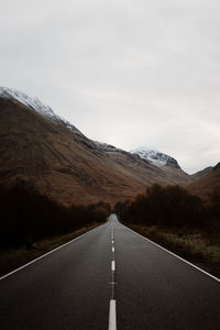 Road leading towards mountains against sky