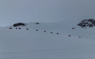 A group of snowmobiles following a guide on rugged mountain terrain