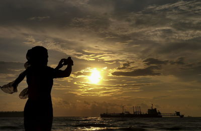 Silhouette woman photographing sea against sky during sunset