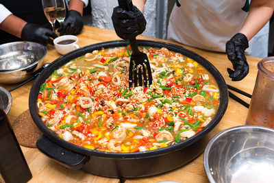 A girl is stirring paella with a black plastic spatula. a large paella bowl on the table