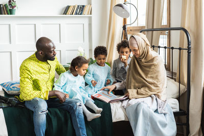 Family looking at book on bed in home