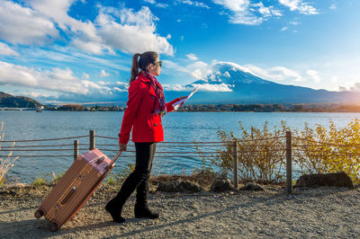 Full length of woman with luggage standing by lake kawaguchi holding map