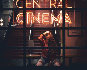 Young woman in illuminated building seen through window at night