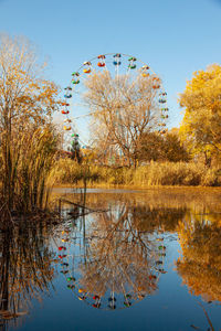 Ferris wheel with a reflection in the blue water of the lake. spring amusement park