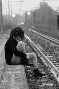 Woman sitting at railway station by track