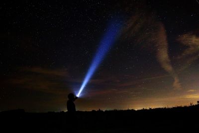 Silhouette person with laser light against sky at night