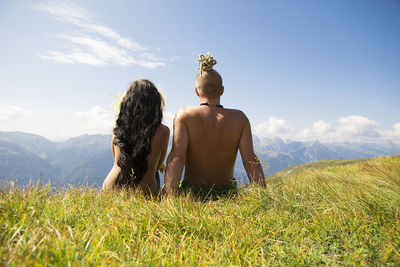 Rear view of shirtless man sitting on grass against sky