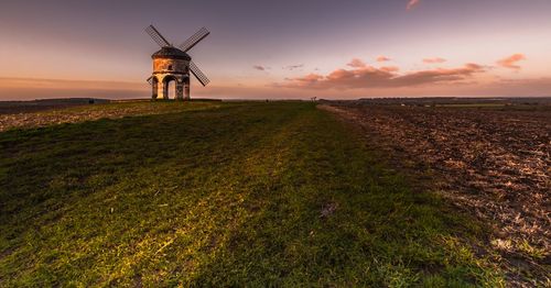 Traditional windmill on field against sky during sunset