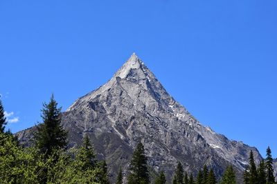Low angle view of trees on mountain against clear blue sky