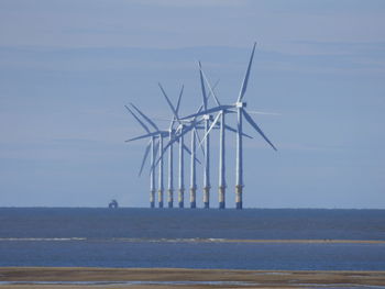 Wind turbines in sea against blue sky