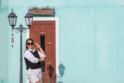 Full length of a smiling young woman standing against door of building