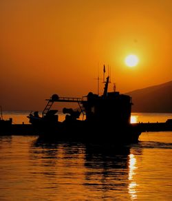 Silhouette ship in sea against orange sky