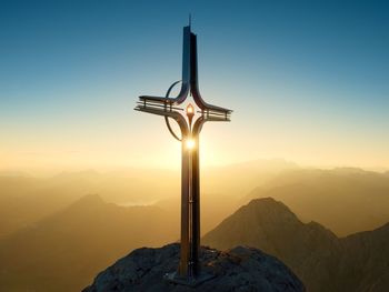 Cross on mountain against sky during sunset