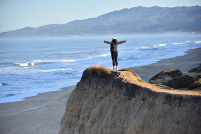 Rear view of woman standing on cliff against sea