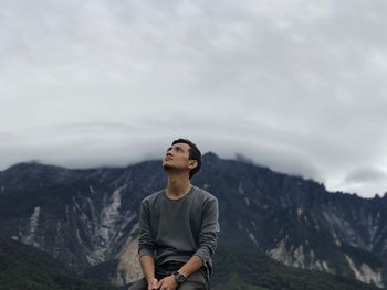Young man sitting against mountains