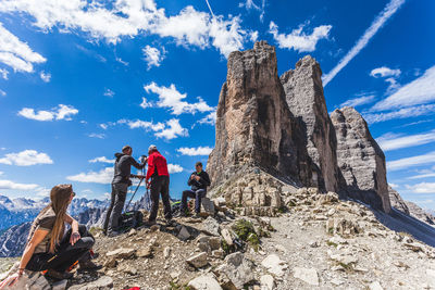 People on rock formation by mountain against sky