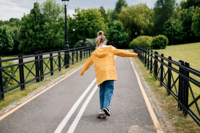 Happy teenage girl learning to ride a skateboard in the city park.