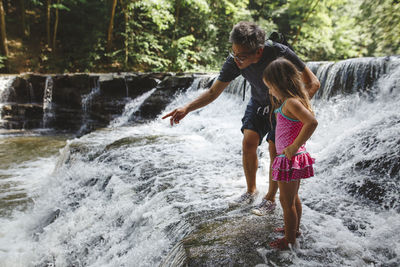 Uncle with girl standing on rock in waterfall