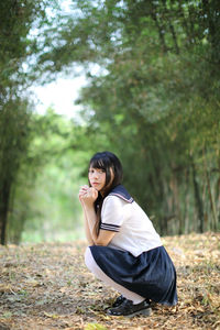 Side view of young woman crouching on land in forest