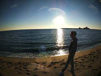 Rear view of man standing on beach against clear sky