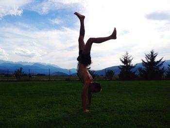 Full length of shirtless man doing handstand on field against sky