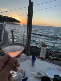 Man holding beer at sea against sky during sunset