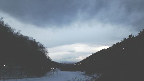 Silhouette trees on snow covered landscape against sky