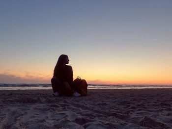 Woman sitting at beach against sky during sunset