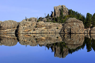 Reflection of rocks in lake against clear sky