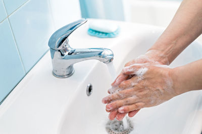 Cropped image of hand touching water from faucet in bathroom