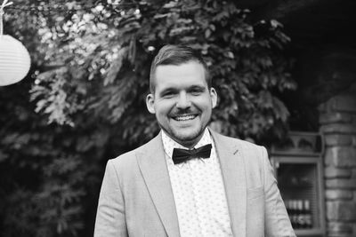 Portrait of young man standing against trees black and white 