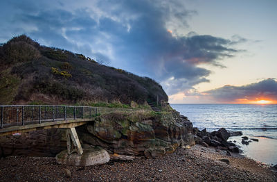 Bridge at beach by sea against sky during sunset