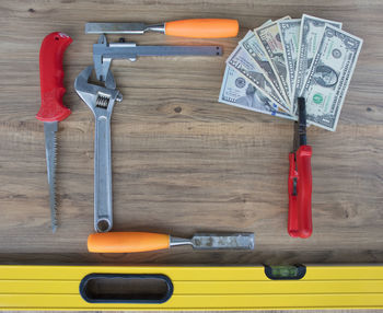 High angle view of paper currencies with work tools on wooden table