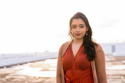 Portrait of young woman standing at beach against sky