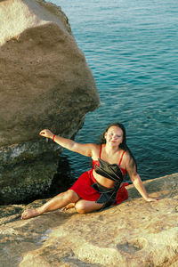 Full length of woman sitting on rock at beach