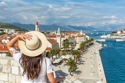 Rear view of woman standing on city walls looking at idyllic seaside town of trogir, croatia