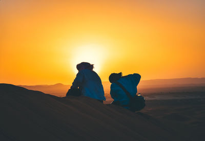 Rear view of men sitting on land against sky during sunset