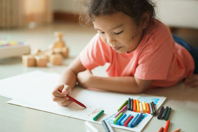 Girl coloring on paper while lying at home