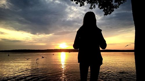 Silhouette woman standing by sea against sky during sunset