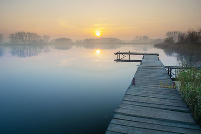 Long wooden jetty on a calm and misty lake during sunset